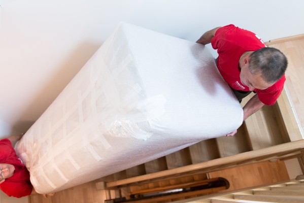 Two Keller Swiss Group employees carry a sofa in overseas packing up a flight of stairs